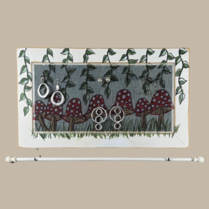 Hand-painted jewelry organizer - Studio Series Mushrooms Design - on a white distressed solid wood frame and a decorative fiberglass screen as the earring holder surface. A matching jewelry bar hangs from the frame.